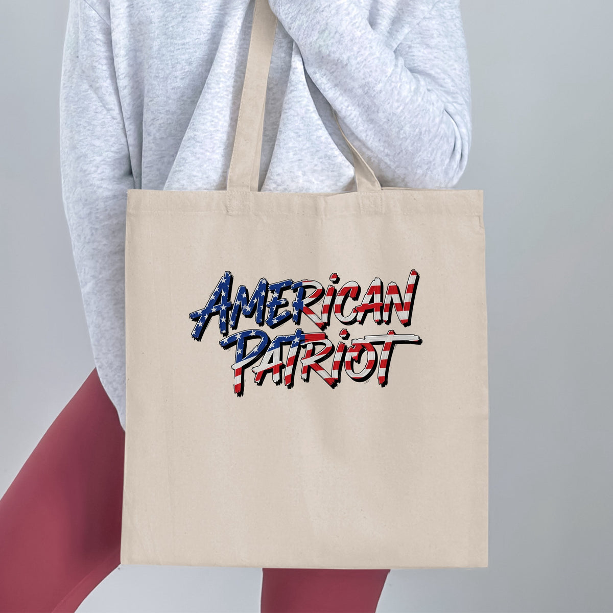 Handheld American Patriot Tote Bag, showing the full flag-filled stacked typography and dark drop-shadow detailing.