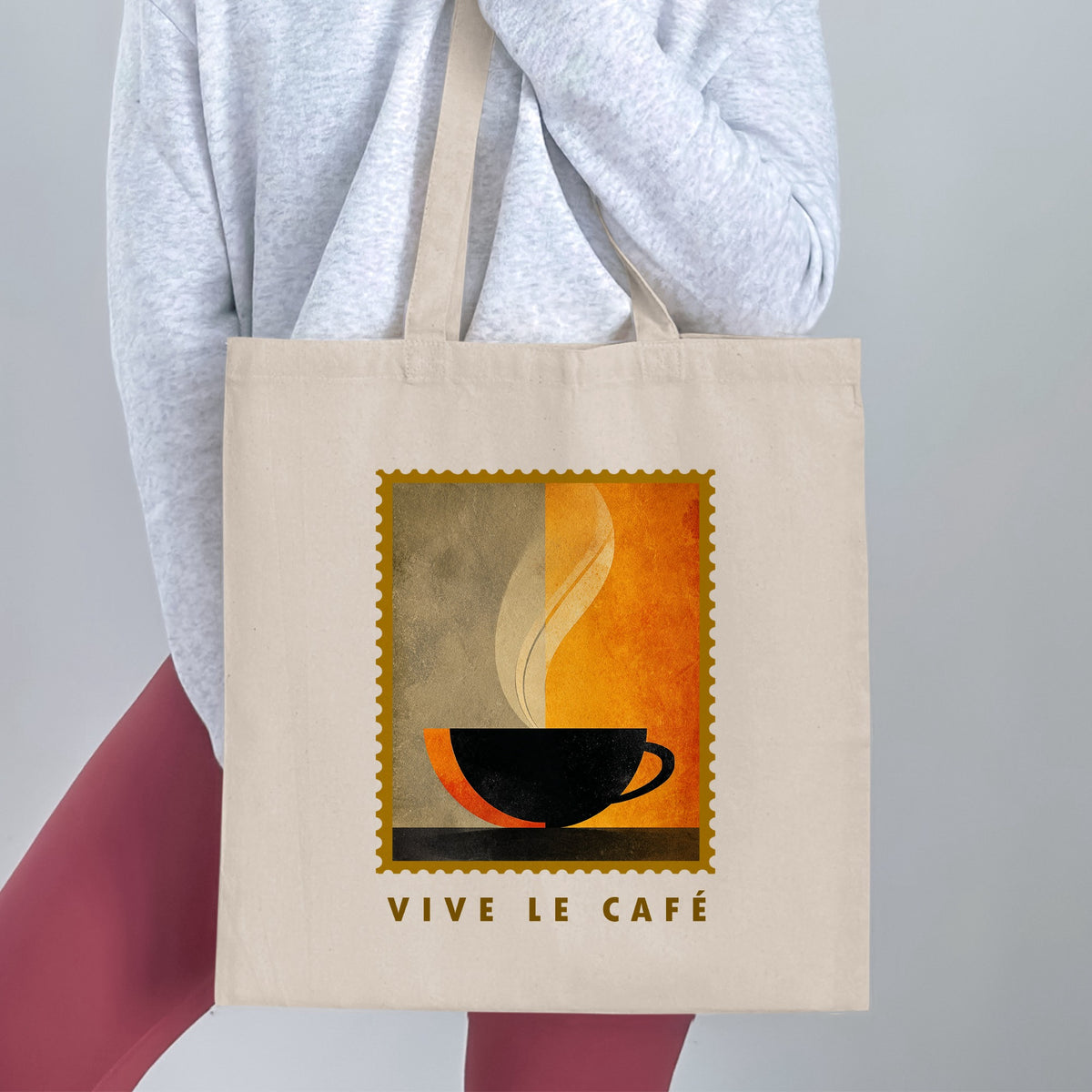 Minimalist Coffee & Steam Tote Bag held by a woman, with black cup silhouette, cream steam, gold border and VIVE LE CAFE lettering.