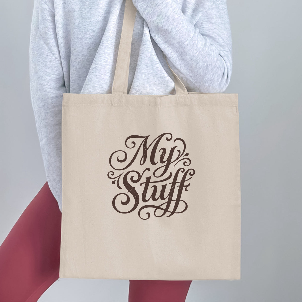 My Stuff Tote Bag handheld, showing the ornate two-line Victorian brown script design across the natural canvas.