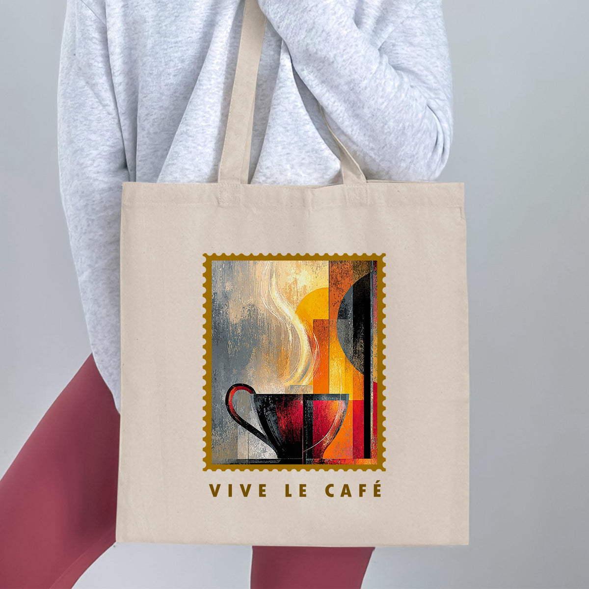 Painterly Steam Tote Bag held by a woman, with charcoal-red cup, sweeping cream steam, gold border and VIVE LE CAFE lettering.
