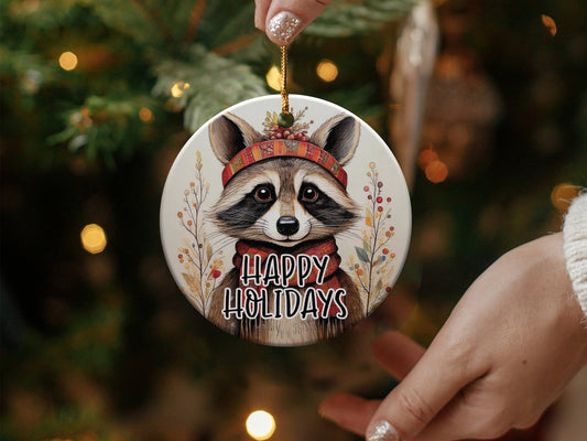Ceramic Happy Holidays ornament featuring a playful raccoon with festive decorations