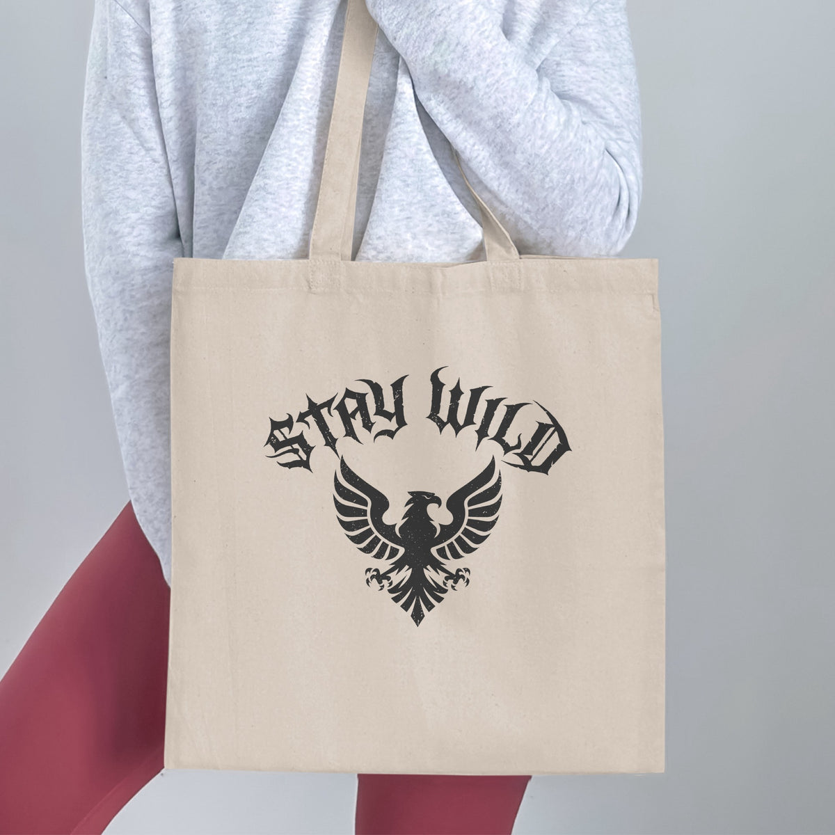 Stay Wild Heraldic Eagle Tote Bag handheld, showing the full blackletter and heraldic eagle design with arched blackletter typography above.