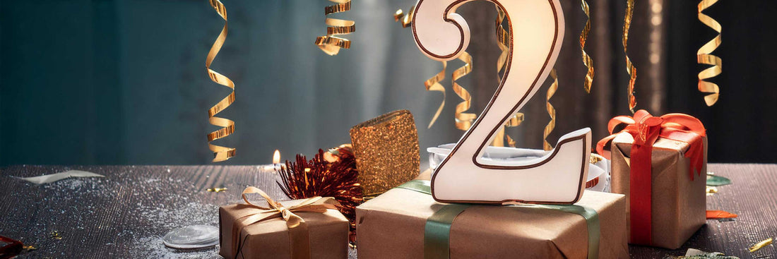 Gold number two decoration surrounded by gift boxes and streamers against a teal backdrop.