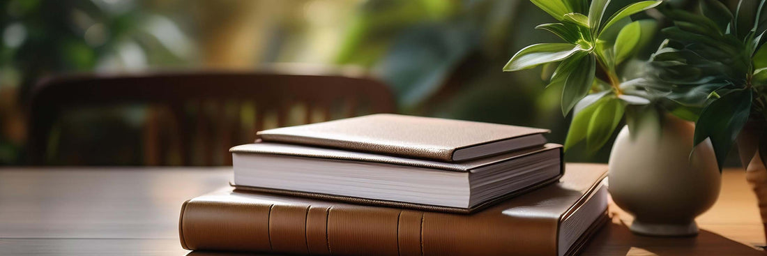 Stack of leather-bound journals styled on a desk with writing accessories and greenery.