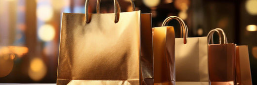 Metallic gold shopping bags with rope handles arranged against a warm golden bokeh background.