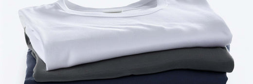 Stack of folded crew-neck t-shirts in white, grey and navy on a white background.