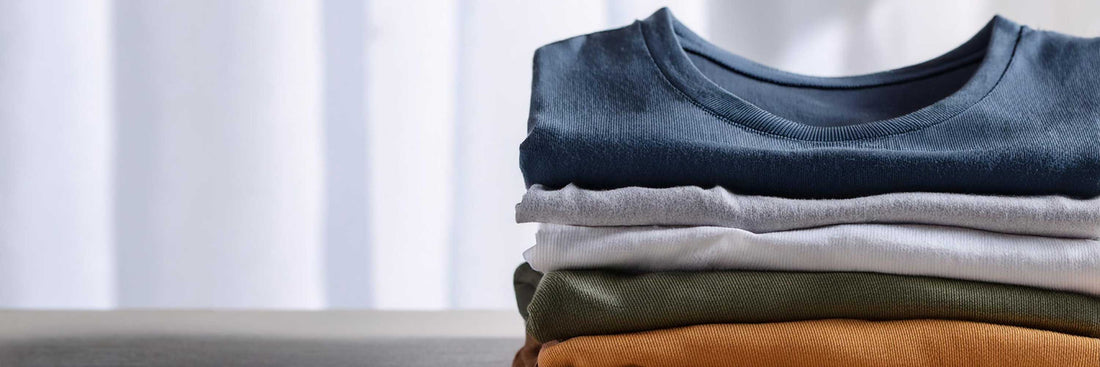 Stack of folded crew-neck t-shirts in navy, grey, white, olive green, and burnt orange.