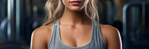 A woman wearing a grey racerback tank top in a gym setting with blurred fitness equipment.