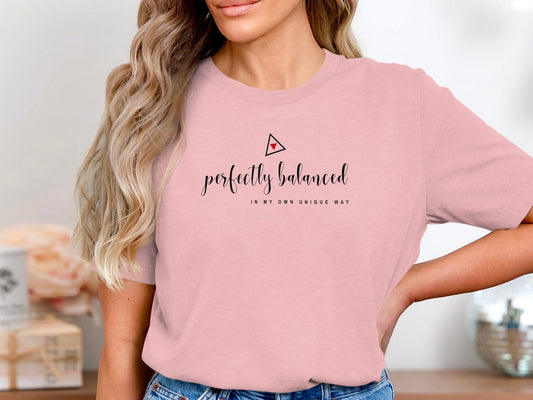 Woman wearing a pink crew-neck affirmation t-shirt featuring Perfectly Balanced typography and geometric graphic.