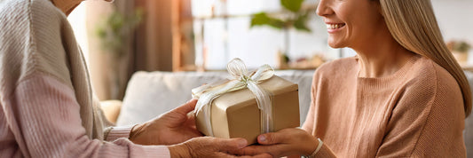A daughter presenting a ribbon-wrapped gift box to her smiling mother in a bright living room.