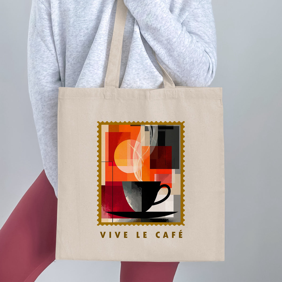 Abstract Coffee Blocks Tote Bag held by a woman, with black cup, layered geometric blocks, gold border and VIVE LE CAFE golden lettering.