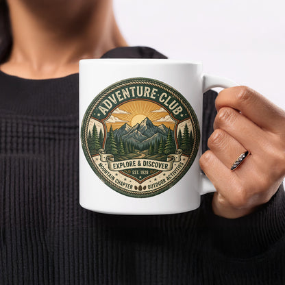 Woman holding Adventure Club 11oz mug featuring forest trail, twin peaks and radiant sunrise emblem.