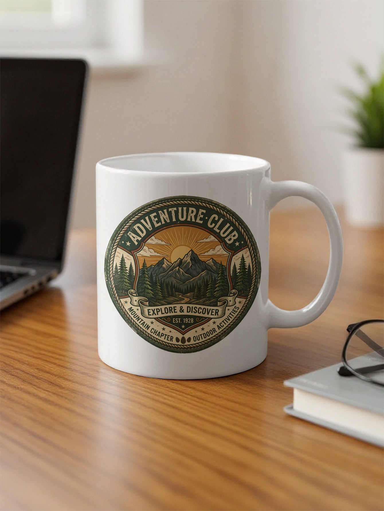 Adventure Club 11oz ceramic mug on office desk with vintage outdoor emblem and rope-bordered mountain design.
