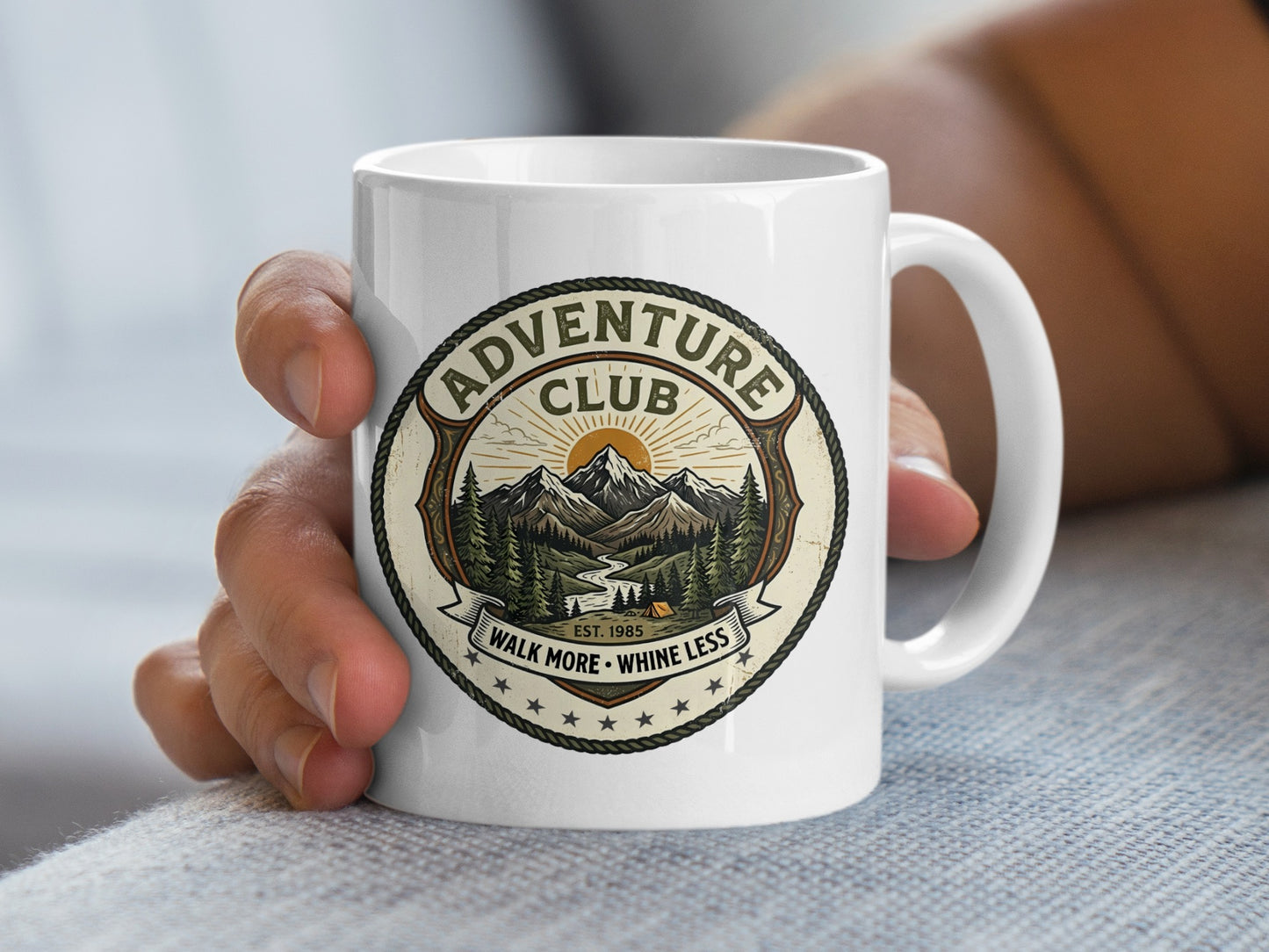 Person holding 11oz Adventure Club mug with a green mountain patch design, forest trails, and hiking motto text.