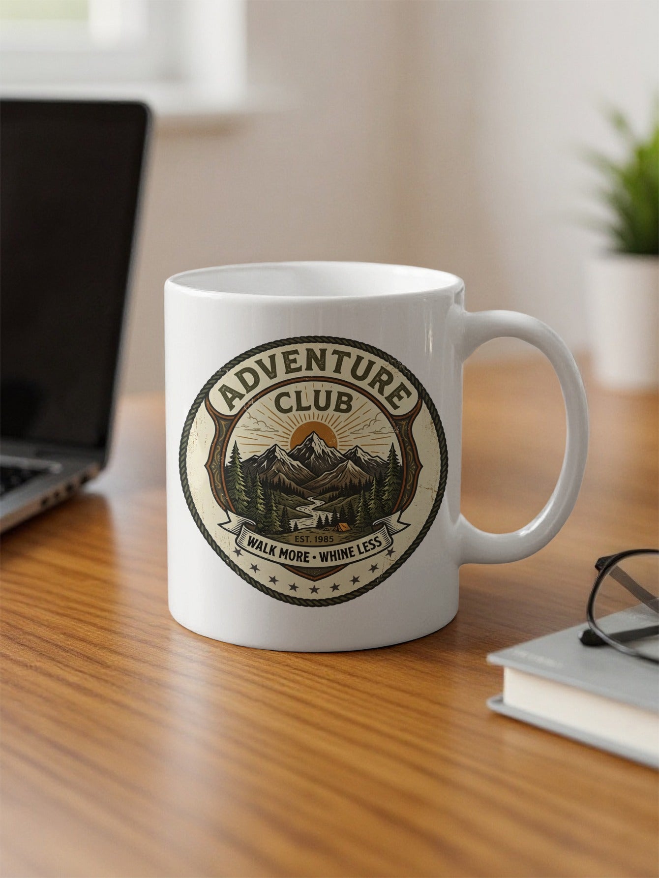 Close-up view of the 11oz Adventure Club ceramic coffee mug design featuring a detailed pine forest emblem placed on a desk.