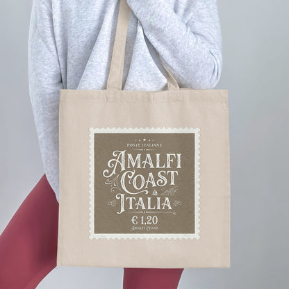 Graphic Amalfi Coast Italia Tote Bag handheld, showing the full AMALFI COAST / ITALIA design and natural canvas body.