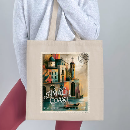 Natural-tone Amalfi Coast Postage Stamp Tote Bag held by a woman, showing coastal architecture, palm tree and elegant white stamp lettering.
