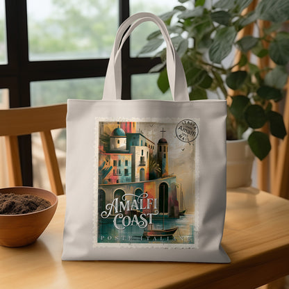 Amalfi Coast Postage Stamp Tote Bag on wooden table with domed towers, harbour boat, warm terracotta and teal tones, and white lettering.