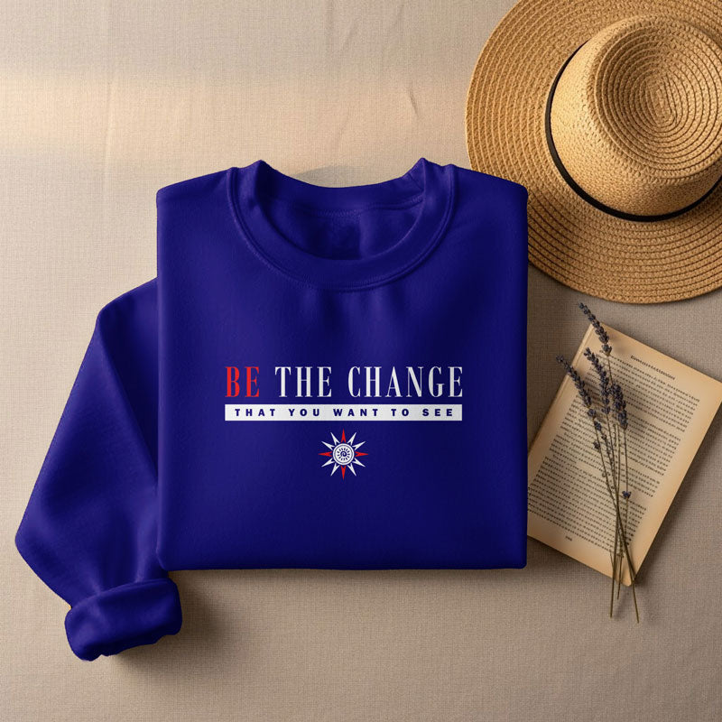Folded royal blue crew neck sweatshirt featuring motivational red and blue typography with a sun emblem, styled with a straw hat and book.