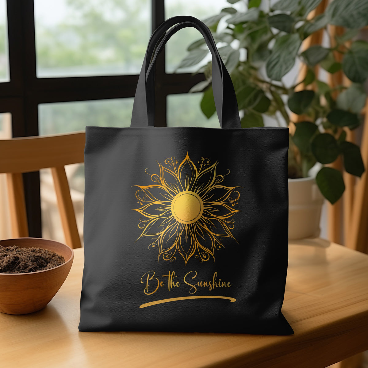 Black Be The Sunshine Tote Bag with golden mandala sun, layered petal detailing and script lettering on wooden table.