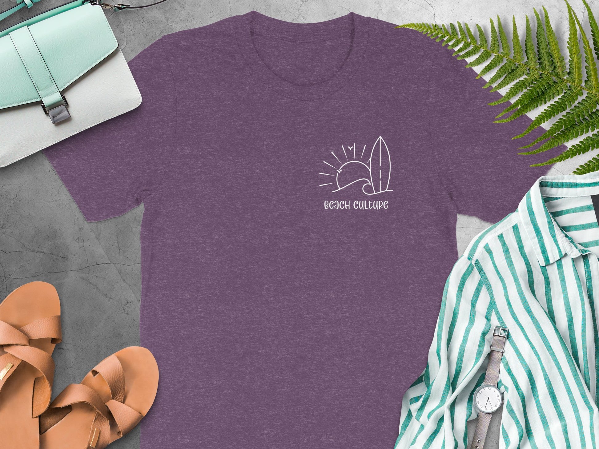Beach Culture purple t‑shirt with a small coastal chest graphic featuring a wave, sun, and surf elements in a simple white line‑art design.