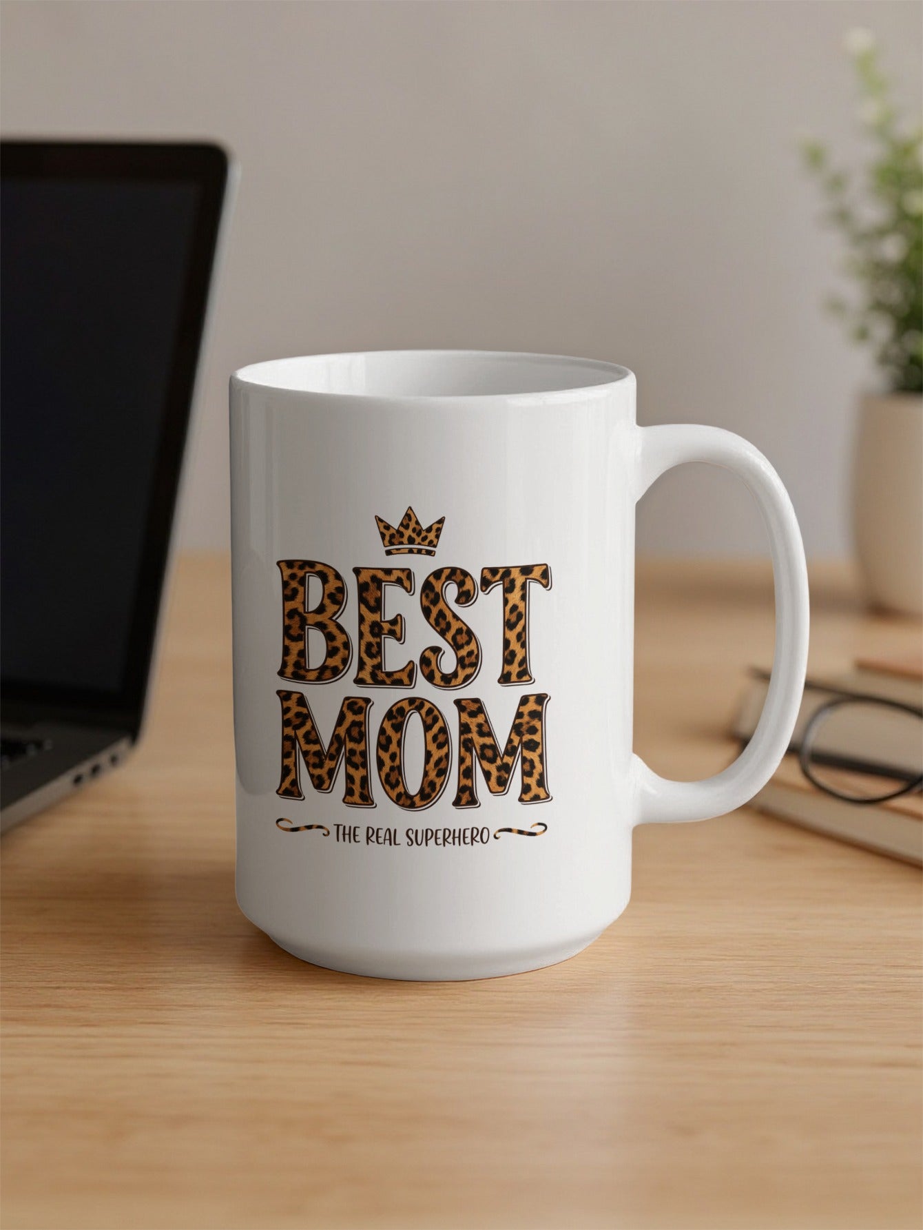 Best Mom The Real Superhero 15oz mug on office desk, bringing bold leopard print style to everyday work coffee breaks.