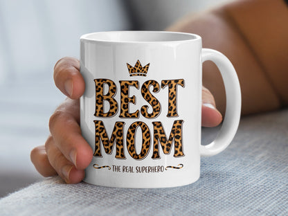 Hand holding Best Mom The Real Superhero mug with leopard print, perfect for daily coffee and heartfelt gifting.