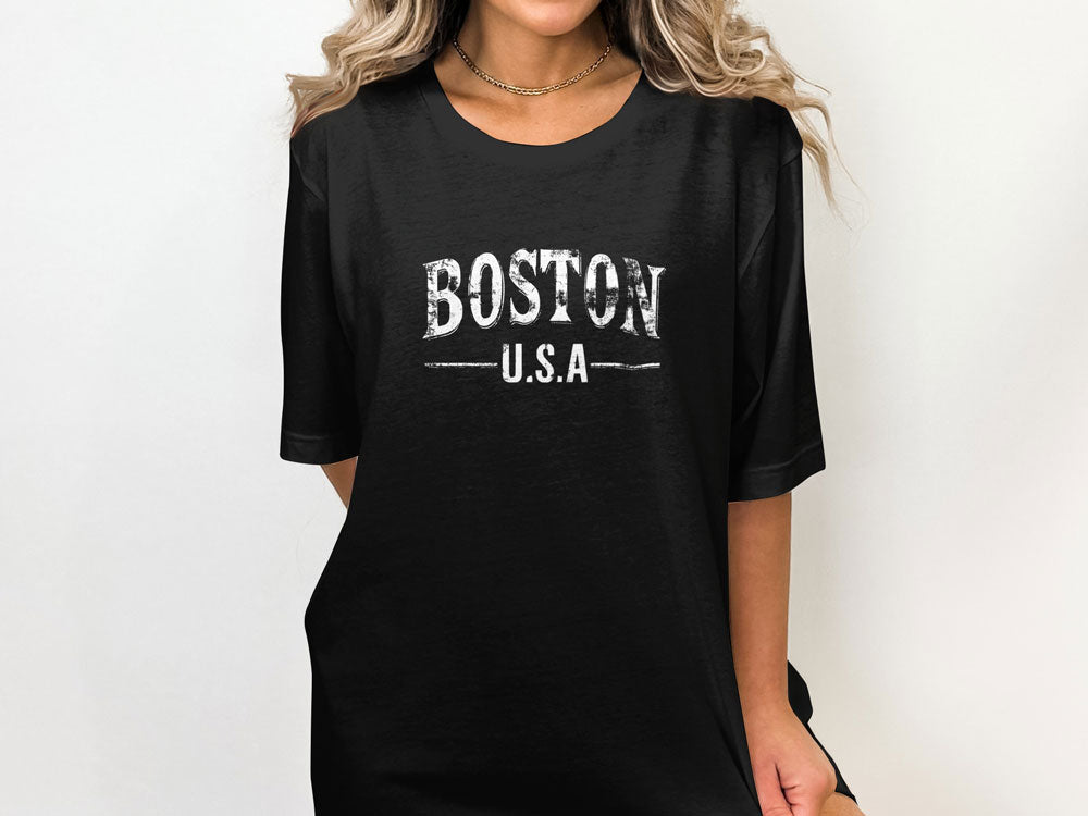Woman wearing a black oversized crew neck t-shirt featuring distressed Boston U.S.A varsity chest graphic with a relaxed streetwear fit.

