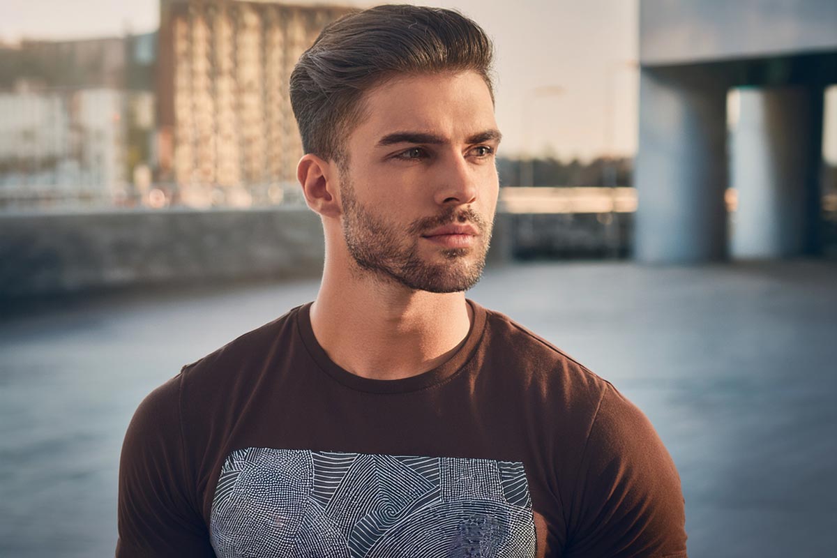 Man wearing dark brown crew neck t-shirt featuring abstract white geometric chest artwork with panel-style design.