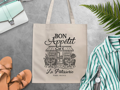 Black line-art Parisian café design with rattan-style chairs, outdoor bistro tables and leafy potted plants on a canvas cotton graphic tote bag.