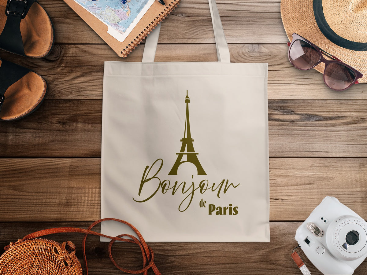 Bonjour de Paris Tote Bag in a lifestyle setting, highlighting the understated Parisian graphic and natural canvas against the muted olive-brown artwork.