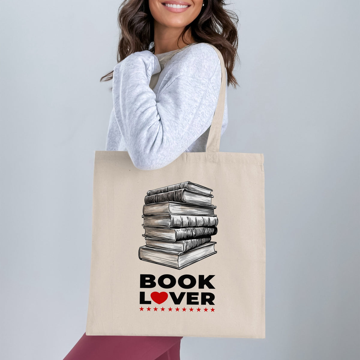 Book Lover canvas tote bag worn over shoulder with hand-drawn book stack, bold lettering, red heart and small red stars.