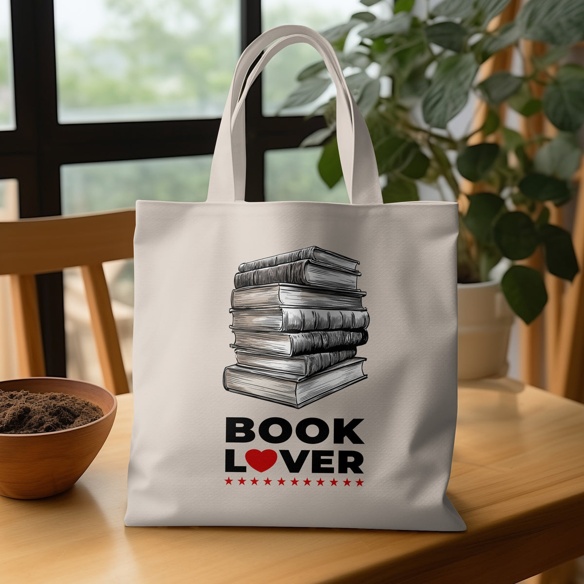 Natural-tone Book Lover Tote Bag on wooden table with uneven stack of books, cross-hatched linework and bold BOOK LOVER black lettering.