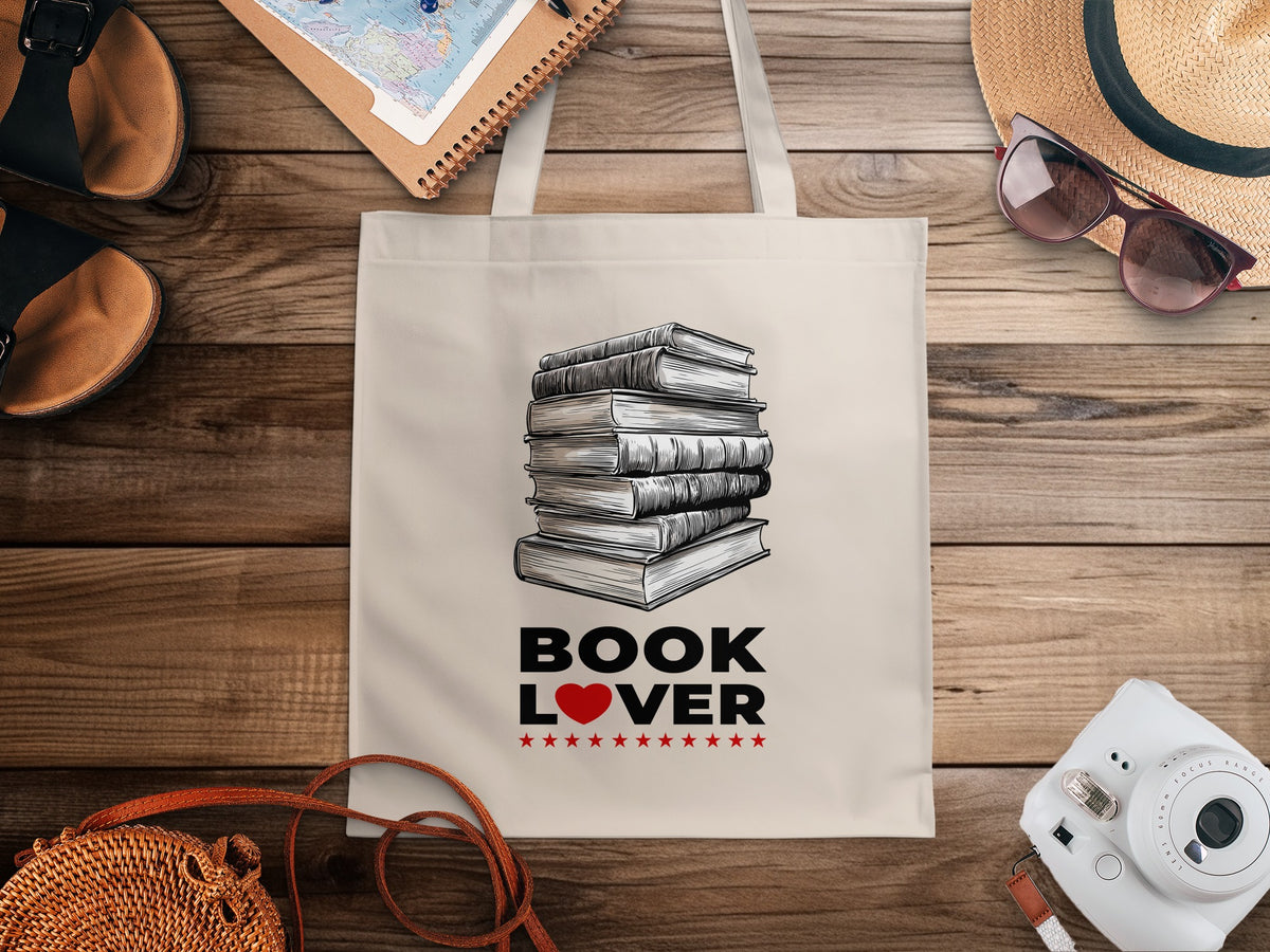 Cream Book Lover canvas tote bag with seven stacked books in detailed monochrome linework, grey shading and visible pages with black lettering and red heart accent.