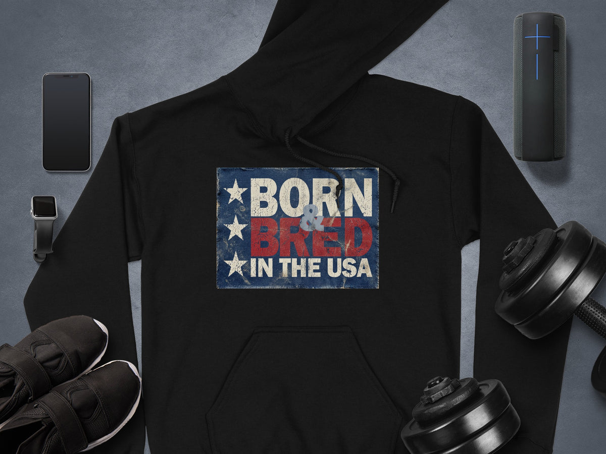 Born & Bred in the USA Hoodie in black, showcasing stacked patriotic text, a weathered blue background and three vertical white stars.