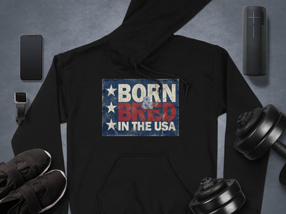 Born & Bred in the USA Hoodie in black, showcasing stacked patriotic text, a weathered blue background and three vertical white stars.
