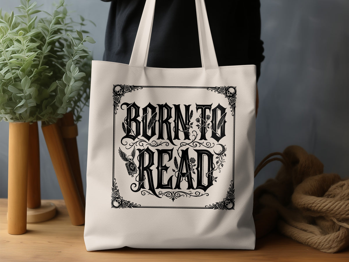 Born to Read graphic tote bag lifestyle display showing gothic lettering, floral sprays, quill feather and decorative skull border.