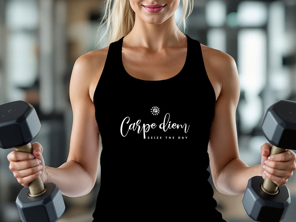 Woman wearing black tank top featuring 'Carpe Diem seize the day' white script graphic, worn at the gym with dumbbells.