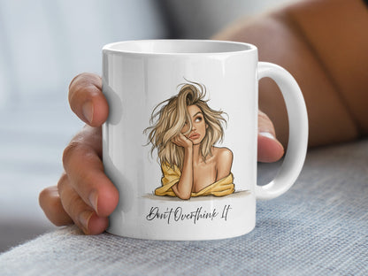 11oz Don't Overthink It Mug held in hand, showing the thoughtful blonde portrait, black sketch linework and light-hearted message.