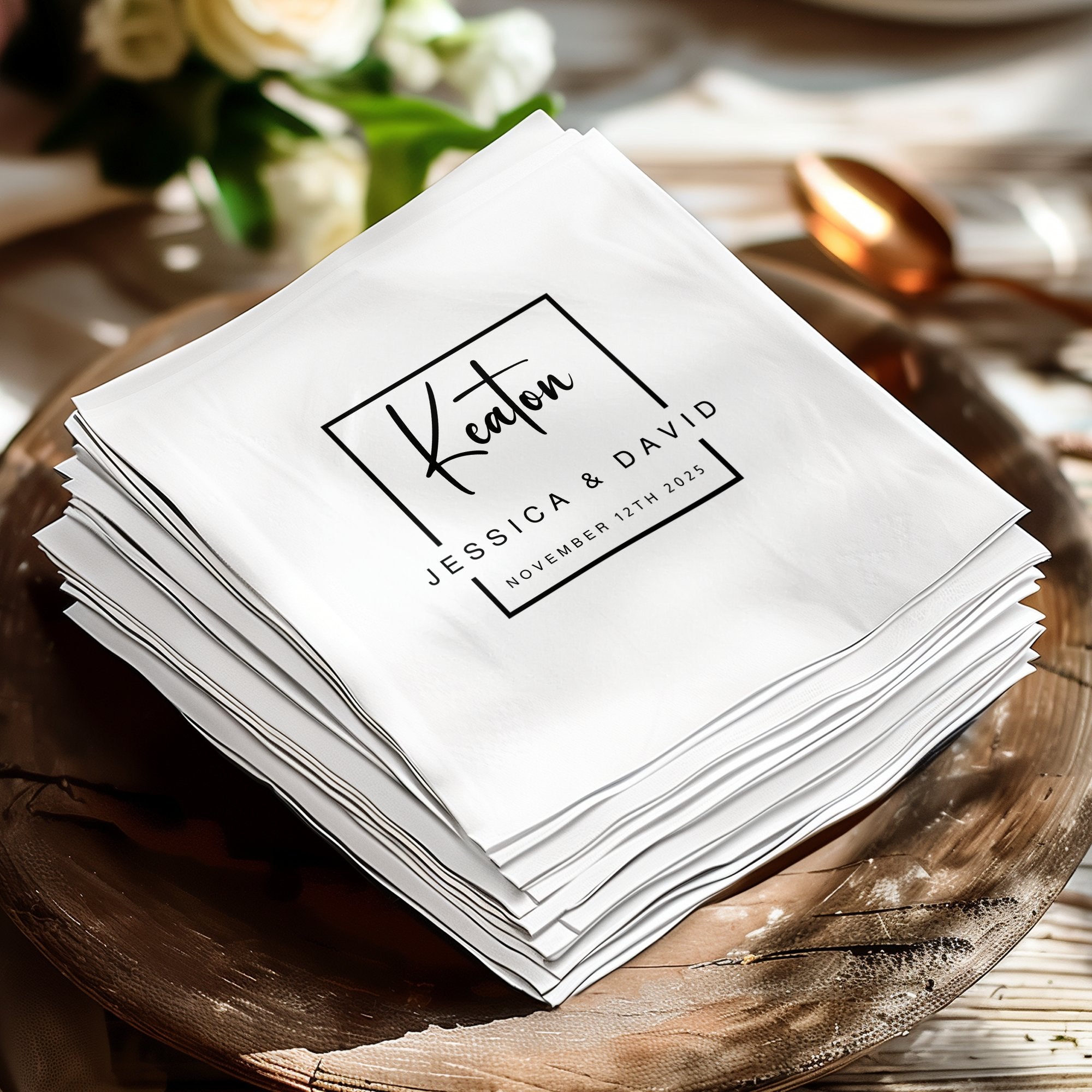 Editorial-style wedding napkins displaying black calligraphic typography, structured borders and custom names.