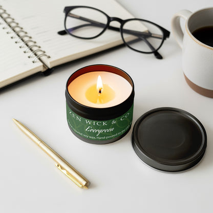 Evergreen scented tin candle 4oz lit with surrounding accessories creating a cozy, woodsy, and calming setting.