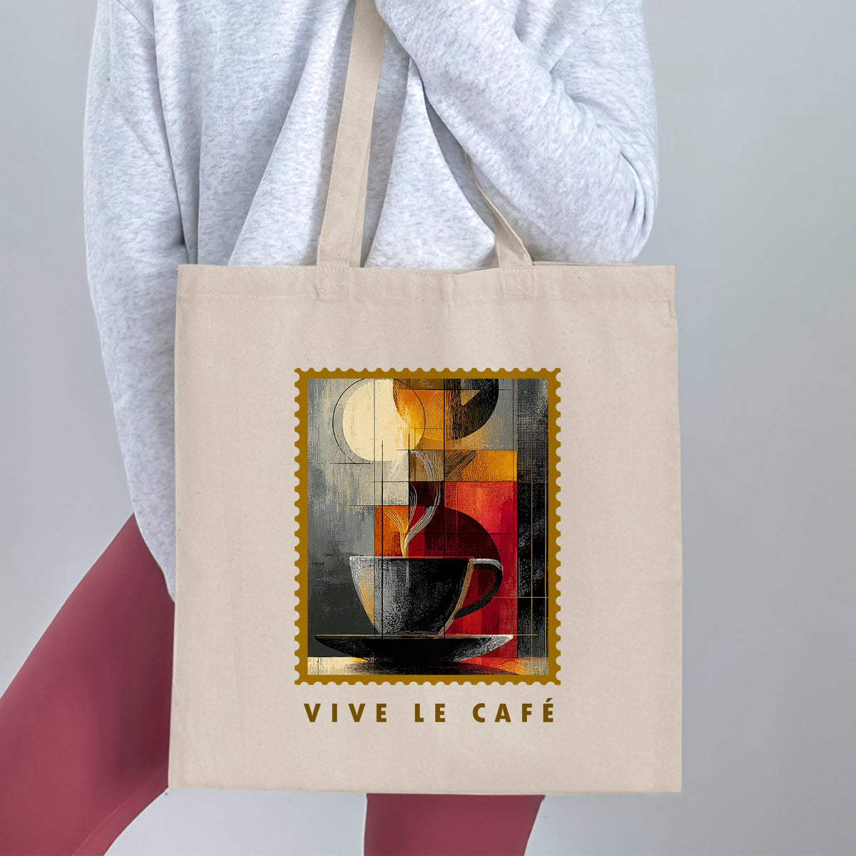 Fragmented Coffee Tote Bag held by a woman, with cubist coffee cup, pale disc, gold border and VIVE LE CAFE lettering beneath.