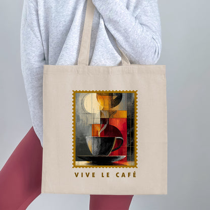 Fragmented Coffee Tote Bag held by a woman, with cubist coffee cup, pale disc, gold border and VIVE LE CAFE lettering beneath.