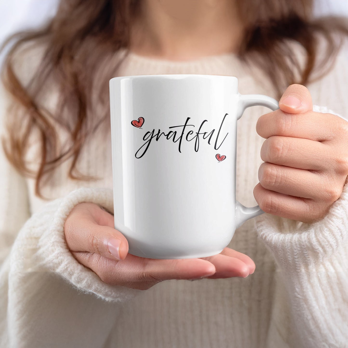 Handheld 15oz white Grateful Heart Mug featuring minimalist black script and two contrasting red heart details with black outlines.