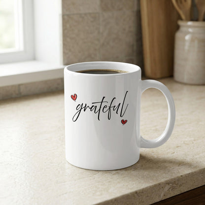 Close-up of Grateful Heart white mug showing the flowing 'grateful' black script and irregular hand-drawn heart heart shapes.