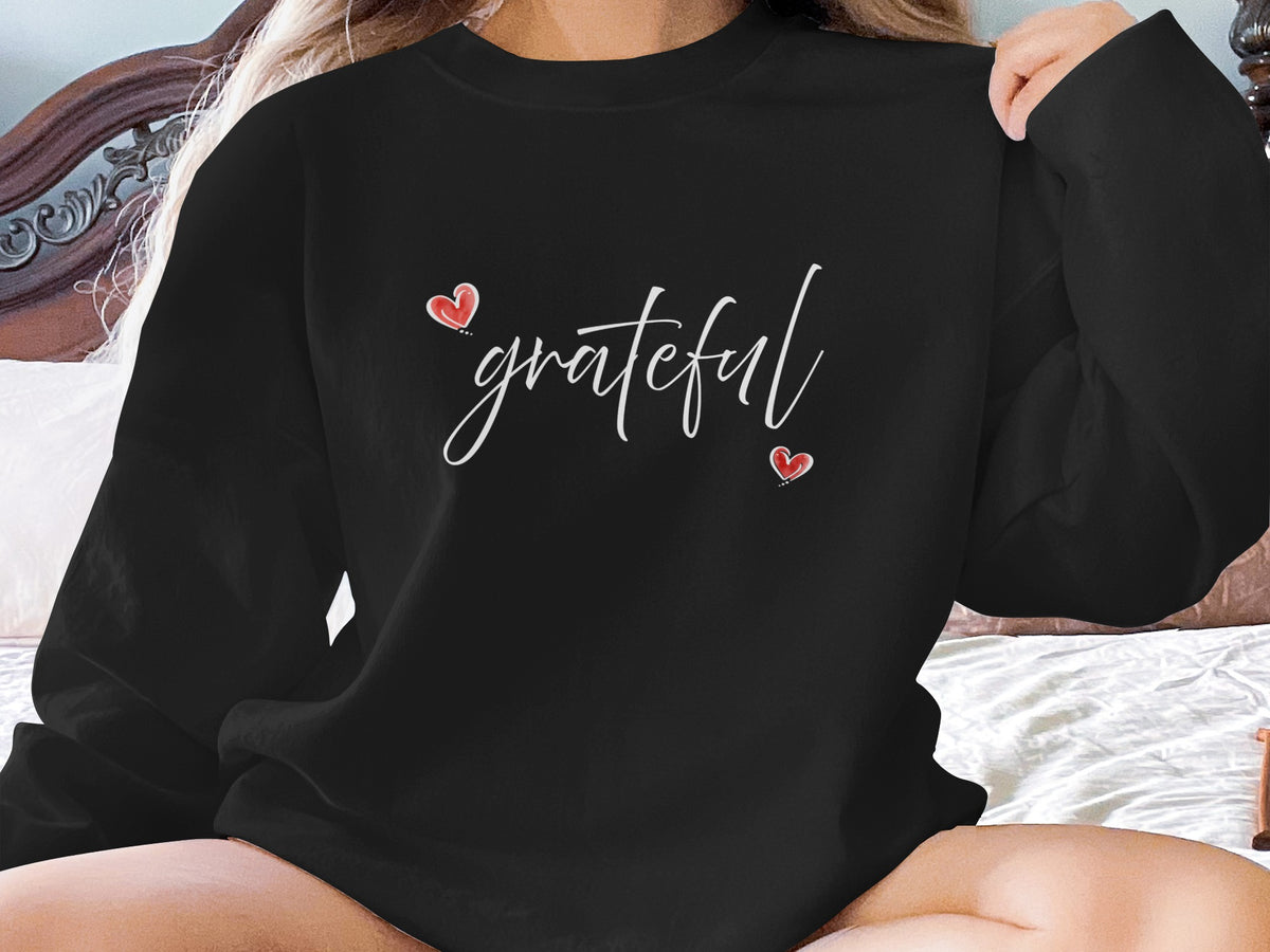 Black Grateful Heart Sweatshirt with flowing white cursive lettering and two small red hearts at centre chest.
