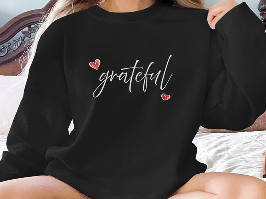 Black Grateful Heart Sweatshirt with flowing white cursive lettering and two small red hearts at centre chest.