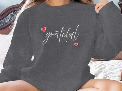 Dark Heather Grateful Heart Sweatshirt with white cursive typography and hand-drawn red hearts in a diagonal layout across the chest.