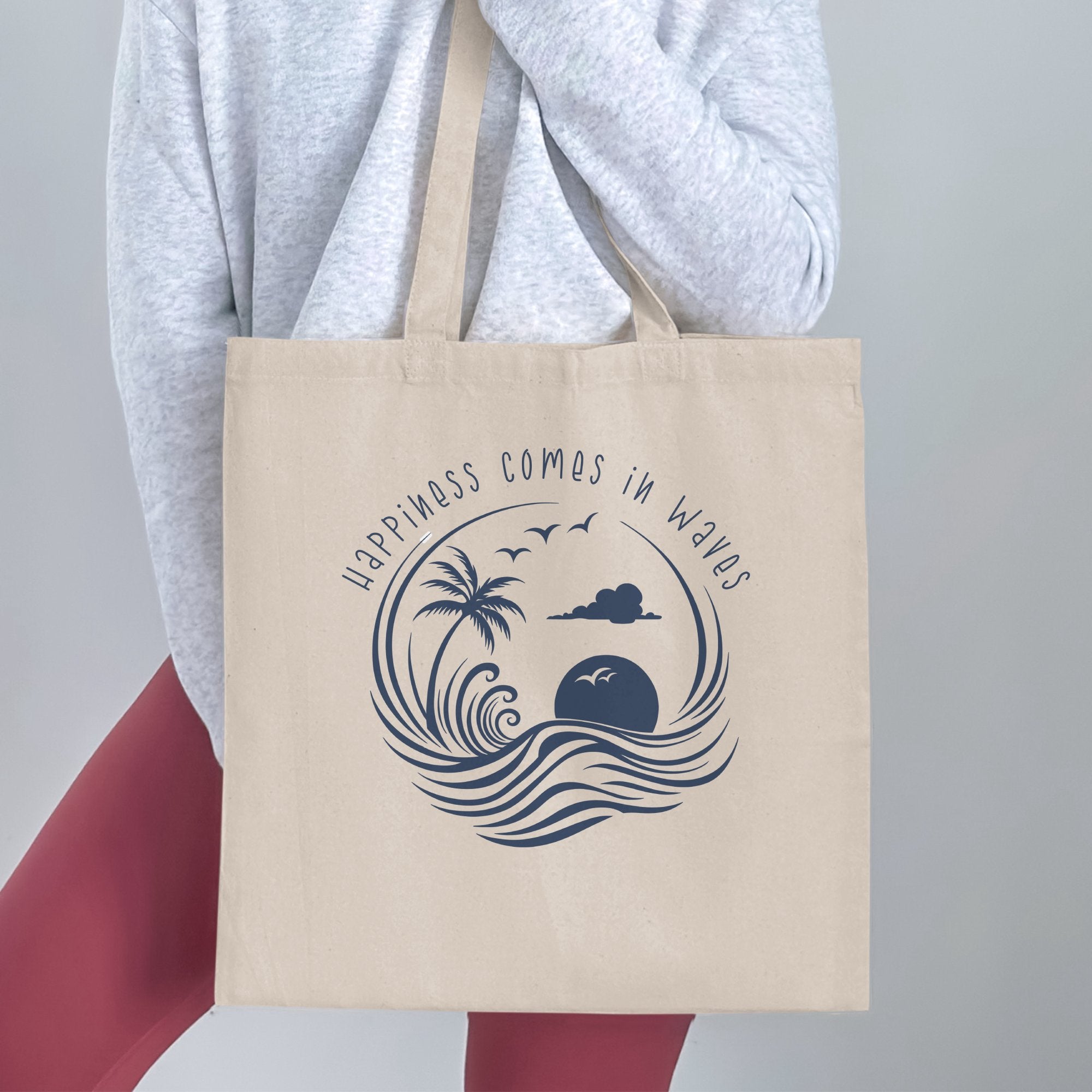 Woman holding a Happiness Comes in Waves Tote Bag featuring a curling wave composition with tropical palm tree and sunburst motif.