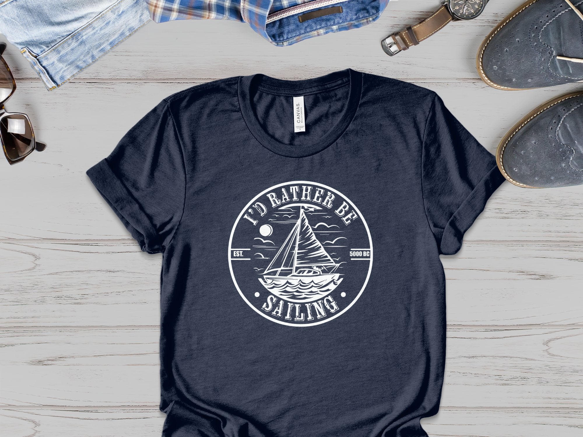 I’d Rather Be Sailing T-shirt with centre-chest nautical badge, sailboat, moon, clouds, and curved white typography design.